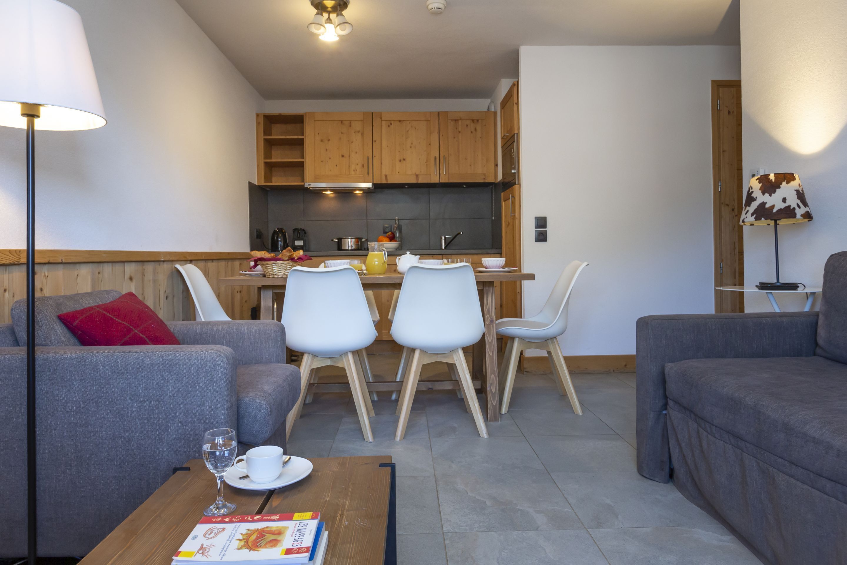 Ein modernes Wohnzimmer mit grauen Sofas, einem Couchtisch mit einer Zeitschrift und einem Essbereich mit weißen Stühlen und einem Holztisch.