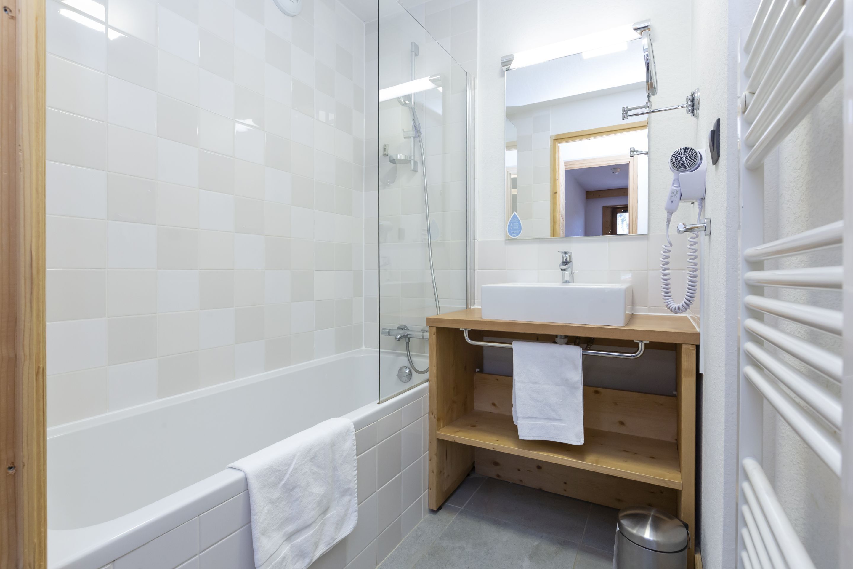 Une salle de bain moderne avec une douche à parois de verre, une baignoire blanche, un meuble-lavabo en bois et un miroir.