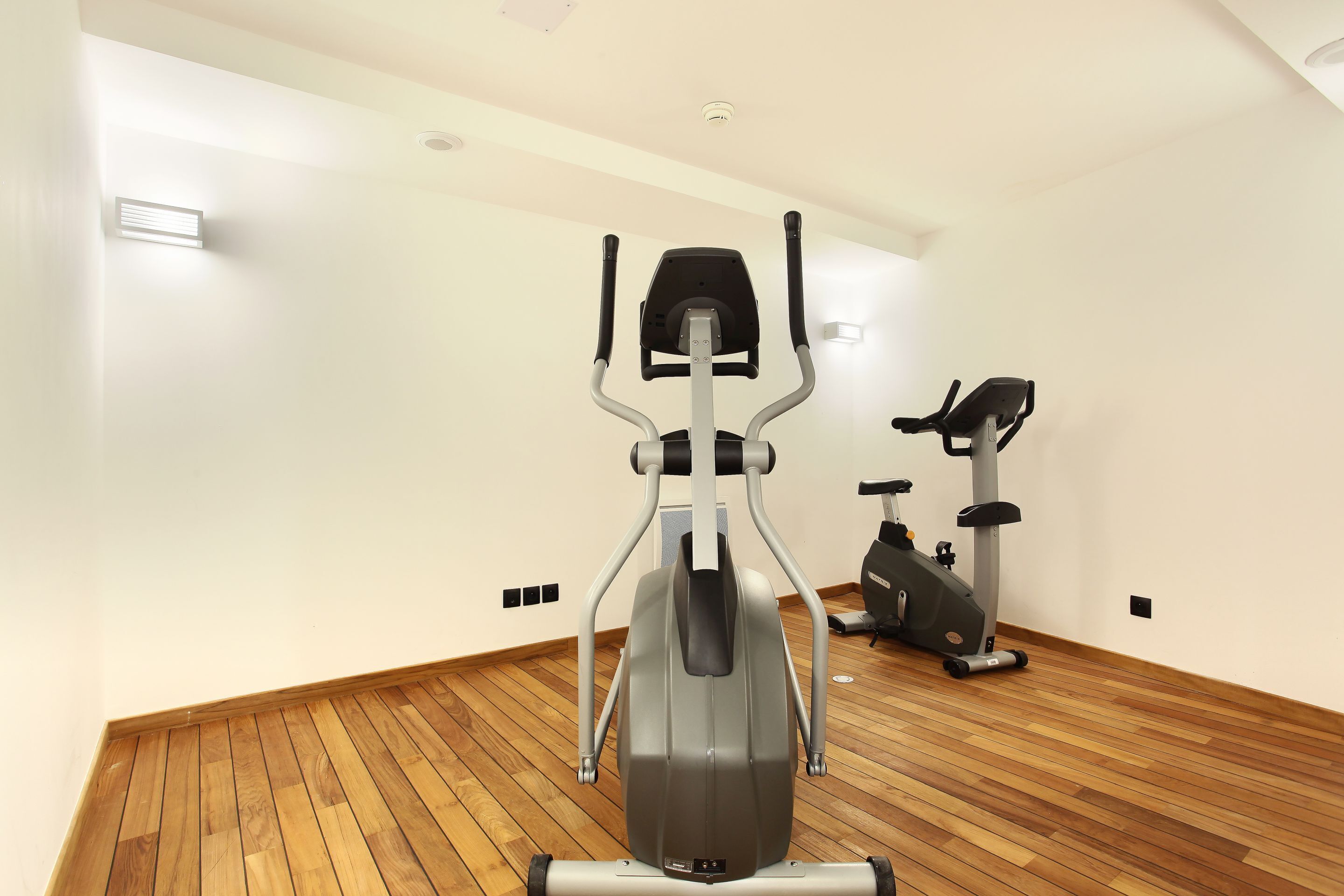 Un gimnasio con equipo de ejercicio, suelo de madera y paredes blancas.