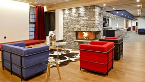 A modern living room with a stone fireplace, red and blue sofas, and a glass coffee table. - Emplacement idéal face à la télécabine | Piscine (Châtel)