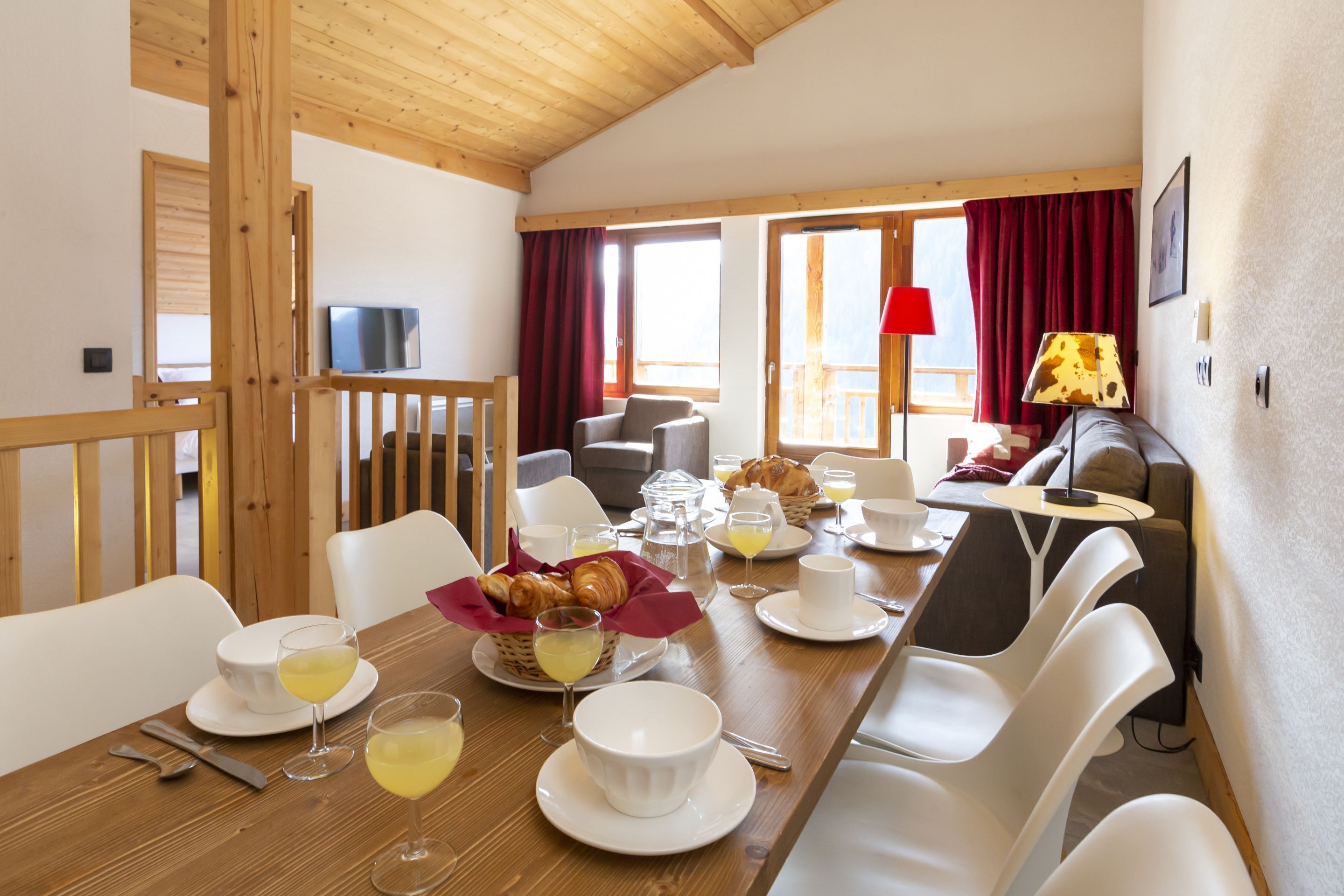 A dining area with a wooden table set for breakfast, white chairs, and a view of the outdoors.