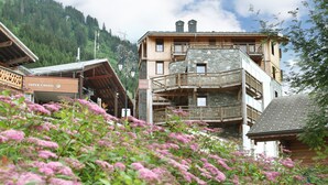 A multi-story building with balconies, a reception area, and a mountain backdrop. - Emplacement idéal face à la télécabine | Piscine (Châtel)