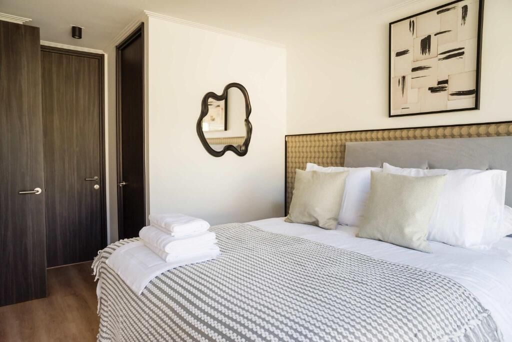 A hotel room with a bed, a mirror, a painting, and a wardrobe.