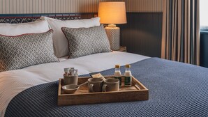 A neatly made bed with patterned pillows, a bedside table with a lamp, and a tray with breakfast items. - The Muddy Fox (Solihull)