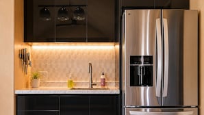 Eine moderne Küche mit Edelstahlkühlschrank, schwarzen Schränken, einer Marmorarbeitsplatte und Holzboden.