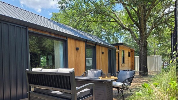 Eine moderne Außenterrasse mit Grill, Sitzgelegenheit und einer Holzkonstruktion mit großen Fenstern.