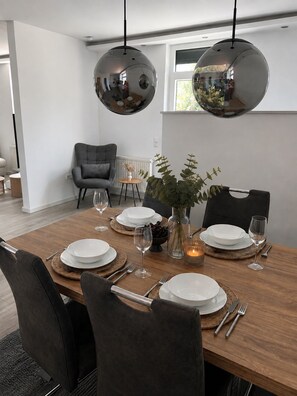 Un coin repas avec une table en bois dressée pour quatre personnes, entourée de chaises, et agrémenté d’un vase de fleurs et de bougies posés sur la table.