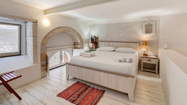 Ein Schlafzimmer mit einem Bett, einem Nachttisch, einer Lampe, einem Fenster und einem roten Teppich.