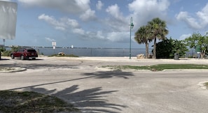 A parking area with a red SUV, a palm tree, and a view of the water. - Charming Pet-Friendly 4BR Cape Coral, minutes from Pine Island and Yacht Club! (Cape Coral)