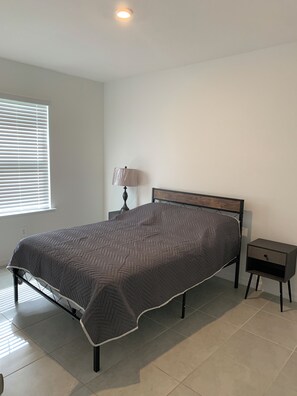 A bedroom with a bed, a nightstand, a lamp, and a window with blinds. - Charming Pet-Friendly 4BR Cape Coral, minutes from Pine Island and Yacht Club! (Cape Coral)