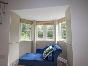 A room with a corner bed, two windows with curtains, a power outlet, and a small plant.