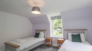Quarto com duas camas de solteiro, janela com vista, luminária no teto e uma pequena mesa de cabeceira de madeira.
