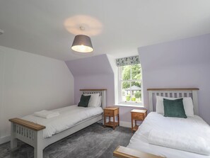 A bedroom with two single beds, a window with a view, a ceiling light, and a small wooden nightstand.