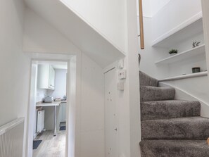 A staircase leading to a landing with a white door, a kitchen area with cabinets, and a radiator. - Station Lodge (Forres)