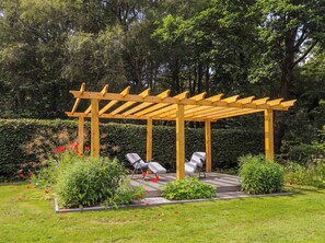 A wooden pergola with seating, surrounded by a garden with various plants and flowers. - Station Lodge (Forres)