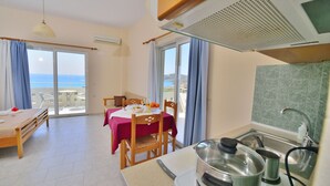 Una habitación con cama, una mesa de comedor, una zona de cocina con fregadero y estufa, y vista al mar.