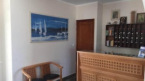 Un área de recepción con un banco de madera, una pintura de veleros y una estantería con objetos enmarcados.