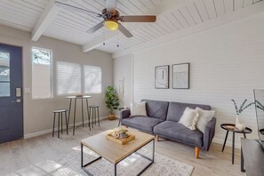 A modern living room with a grey sofa, a coffee table, a ceiling fan, and a dining area with a small table and chairs. - Remodeled Courtyard Apt w/King Bed, In-Unit W&D (Albuquerque)