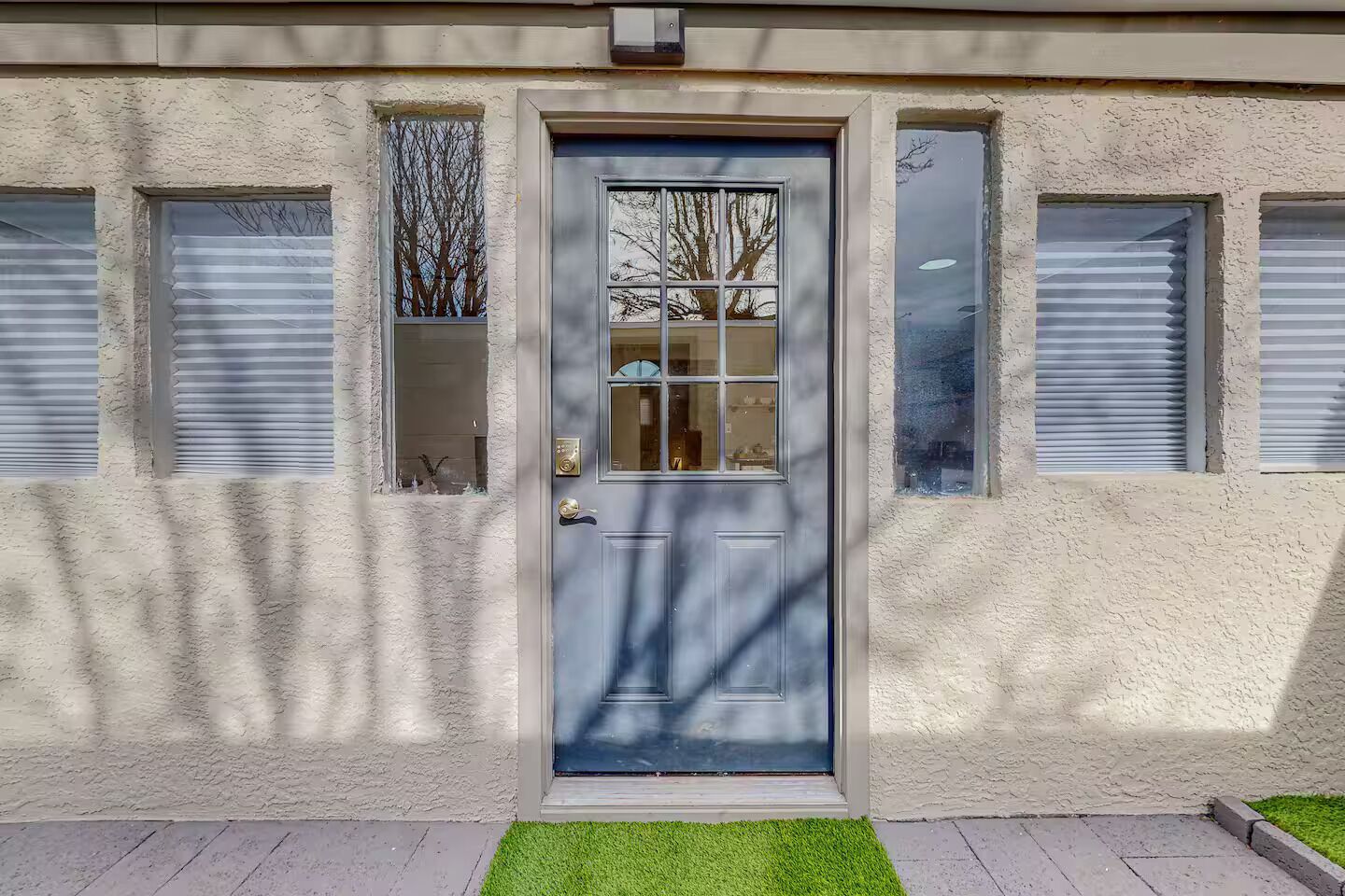 Eine Gebäudefassade mit einer blauen Tür, zwei Fensterläden und einem kleinen Grasstück davor.