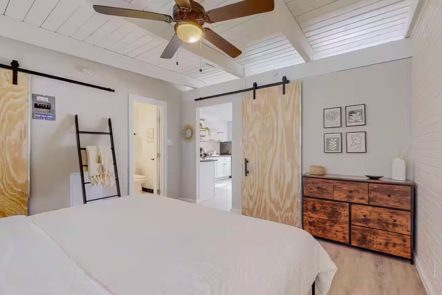 Ein Schlafzimmer mit einem Bett, einem Deckenventilator, einem Kleiderschrank und einer Küchenzeile im Hintergrund.