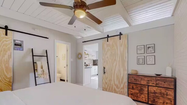Een slaapkamer met een bed, een plafondventilator, een kledingkast en een kitchenette op de achtergrond.