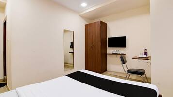 A bedroom with a bed, a wardrobe, a desk with a chair, and a TV.