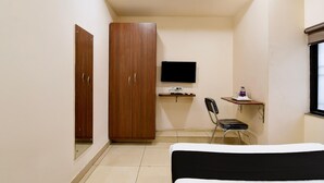 A bedroom with a bed, a wardrobe, a desk with a chair, a television, and a window.