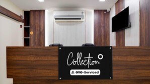 Un comptoir d’accueil avec une pancarte indiquant « Collection OYO – Services inclus », un téléviseur fixé au mur et un appareil de climatisation.