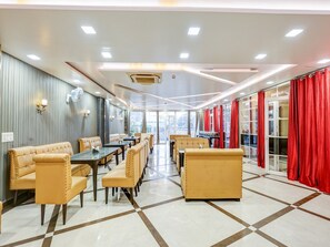A modern dining area with booths and tables, a patterned floor, and a view through large windows. - Deluxe Kathauta Lake Formerly Shivanya (Lucknow)