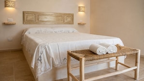 A neatly made bed with a white bedspread and lace trim, a wooden bench with rolled towels, and two wall-mounted light fixtures. - Biancolivo (Ceglie Messapica)
