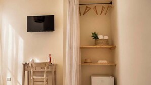 A room with a TV mounted on the wall, a small table with a chair, a mini fridge, and a shelf with items. - Biancolivo (Ceglie Messapica)