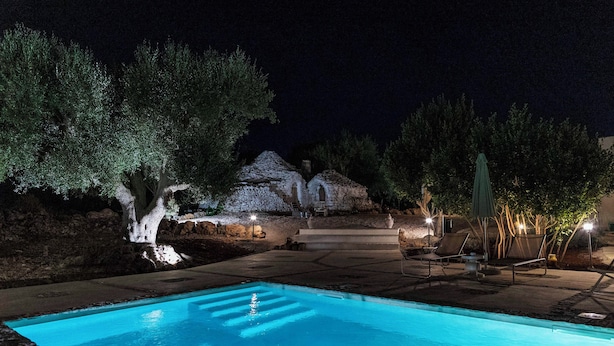 A swimming pool with steps leading into it, surrounded by trees and a stone building with lights. - Biancolivo (Ceglie Messapica)