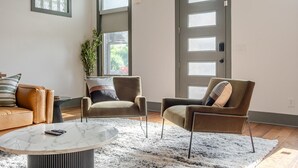 A living room with a brown leather sofa, two armchairs, a marble coffee table, a large window, and a door with frosted glass panels. - Stylish 3BR in Fountain Square Pool, Firepit, Bocce Court + Golden Tee (Indianapolis)
