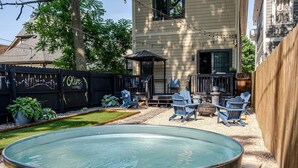 A backyard with a hot tub, outdoor seating, and a wooden deck. - Stylish 3BR in Fountain Square Pool, Firepit, Bocce Court + Golden Tee (Indianapolis)