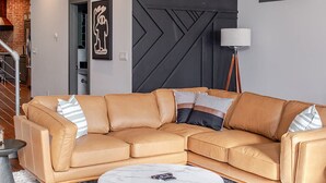 A modern living room with a sectional sofa, a round coffee table, and a black accent wall. - Stylish 3BR in Fountain Square Pool, Firepit, Bocce Court + Golden Tee (Indianapolis)