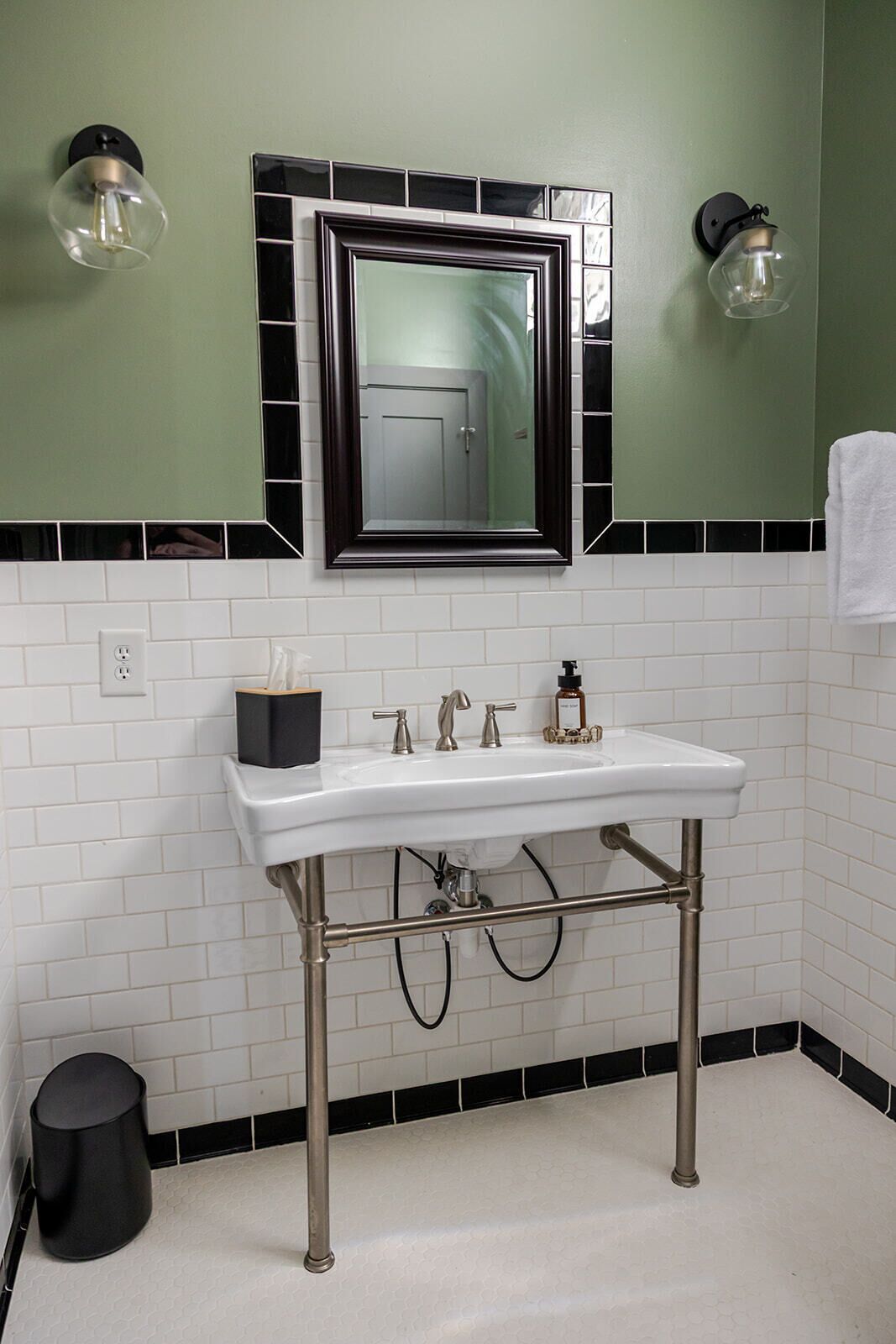 Un baño con un lavamanos blanco, salpicadero de azulejos blanco y negro y dos luminarias empotradas.