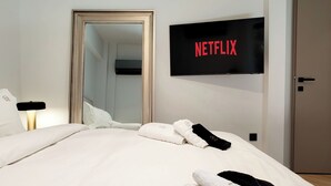 A hotel room with a bed, a TV mounted on the wall, a door, and a mirror. - Designer Flat in Voula Center (Voula)