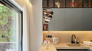 A modern kitchen with a large window, a pendant light, and a view of greenery outside. - Designer Flat in Voula Center (Voula)