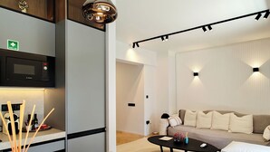 A modern living room with a sofa, coffee table, and a kitchen area with a microwave. - Designer Flat in Voula Center (Voula)