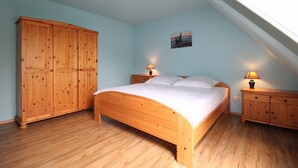 Ein Schlafzimmer mit einem hölzernen Bett, Nachttischen, einem Kleiderschrank und einer schrägen Decke.