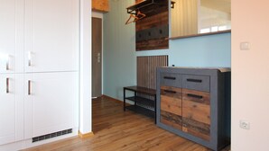 Ein Zimmer mit weißen Schränken, einer Holzbank, einer Pendelleuchte und einem Wandhaken für Kleidung.