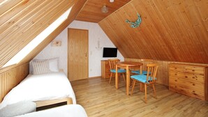 Un dormitorio acogedor en el ático con cama, escritorio y silla, paredes de madera y techo inclinado.