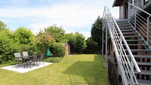 Un patio trasero con una terraza, una escalera y un cobertizo pequeño.