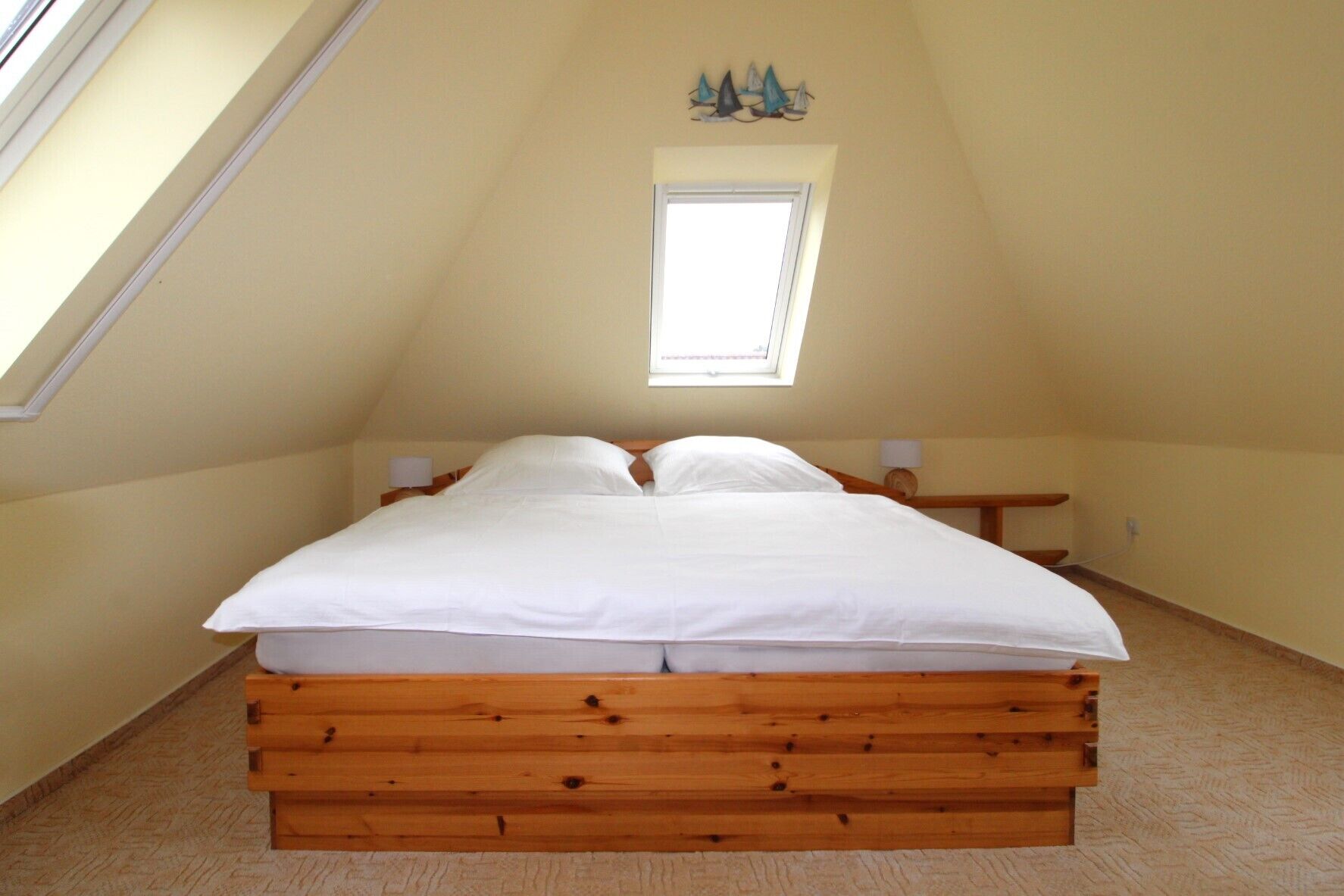 A bedroom with a sloped ceiling, a single bed, a small bedside table, a nightstand, a window, and a decorative wall piece.