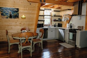 A wooden interior with a dining table and chairs, a kitchen with appliances, and a painting on the wall. - Riv-A-Frame on the Doe River in Elizabethton, TN (Elizabethton)
