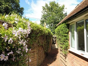 A narrow brick pathway flanked by a wooden fence and a brick wall, leading to a building with a window.