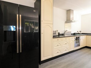 A kitchen with a black refrigerator, cream-colored cabinets, a stainless steel oven, and a microwave on the countertop. - Lucerne Cottage (Dorking)