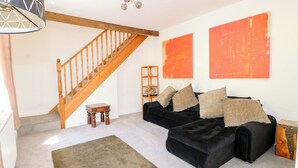 Una sala de estar con una escalera, un sofá negro y dos grandes cuadros naranjas.