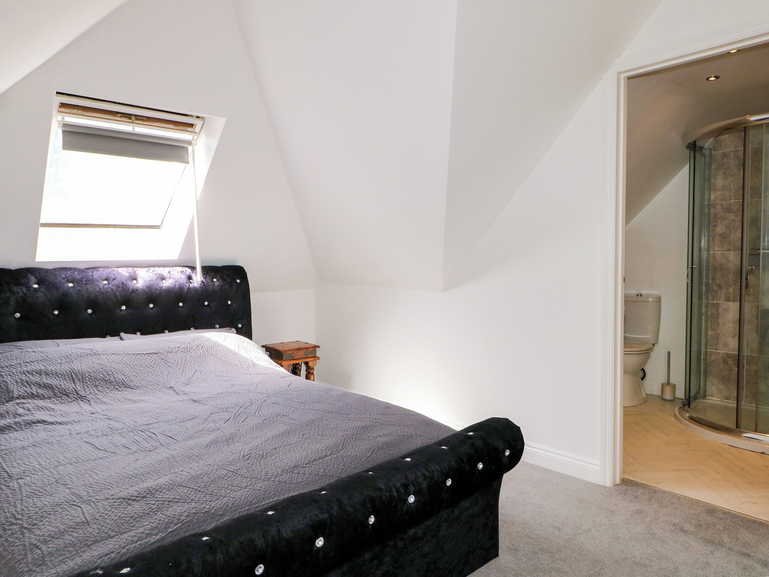 A bedroom with a bed, a small table, a window, and a shower area.