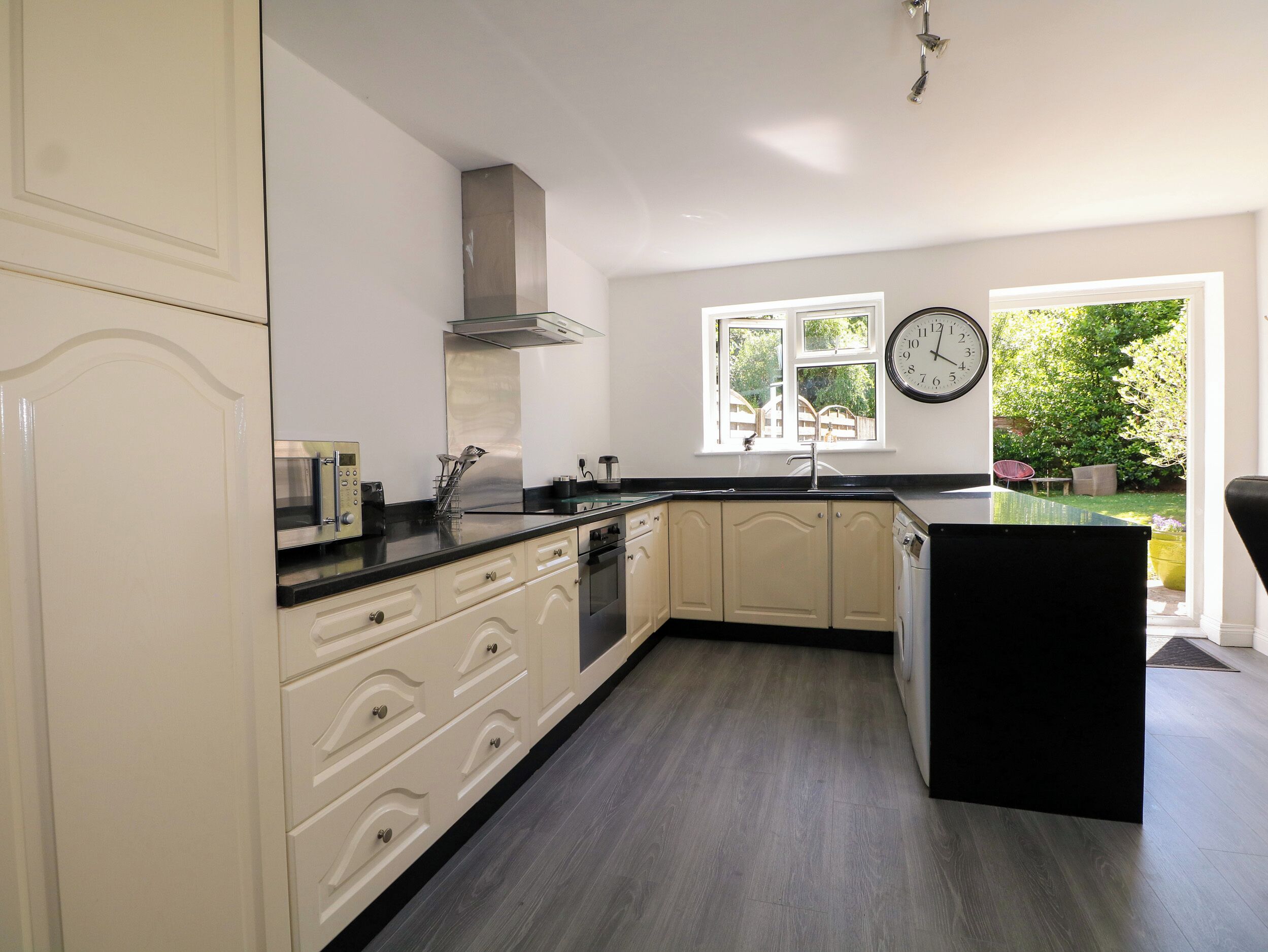 Une cuisine moderne avec des meubles blancs, un plan de travail noir, un four encastré et une fenêtre donnant sur un espace verdoyant.